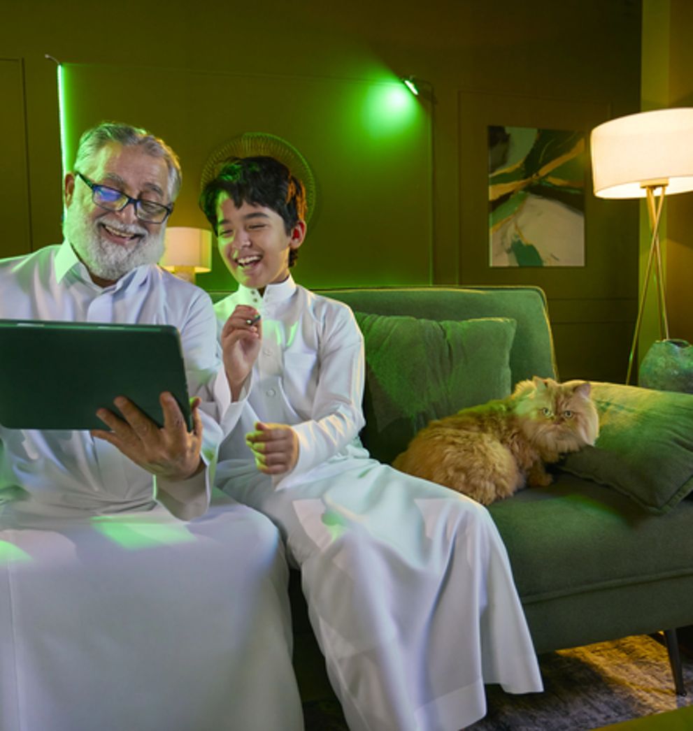 Grandfather and grandson using a tablet at home on Salam postpaid and roaming packages in Saudi Arabia